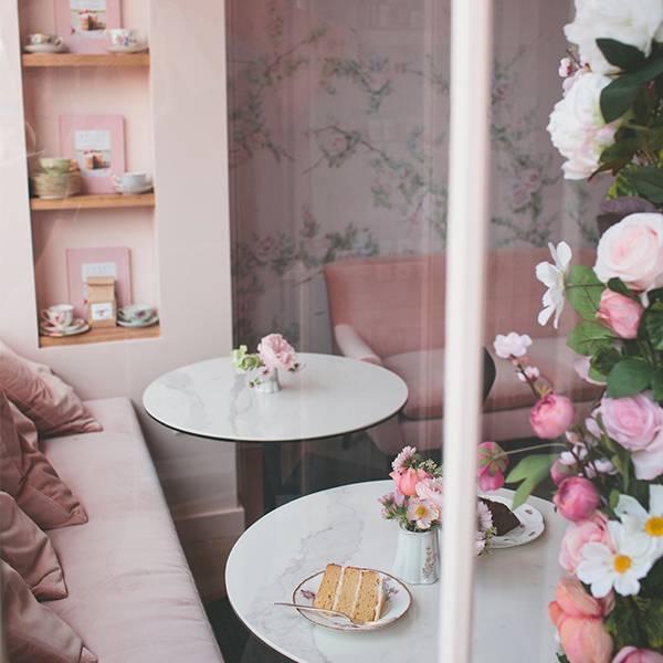 inside of a bakery with a bench and tables with cake and flowers on the table